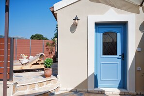 A beige building with a blue door, a small outdoor seating area with a lounge chair and potted plants, and a stone staircase leading to the entrance.