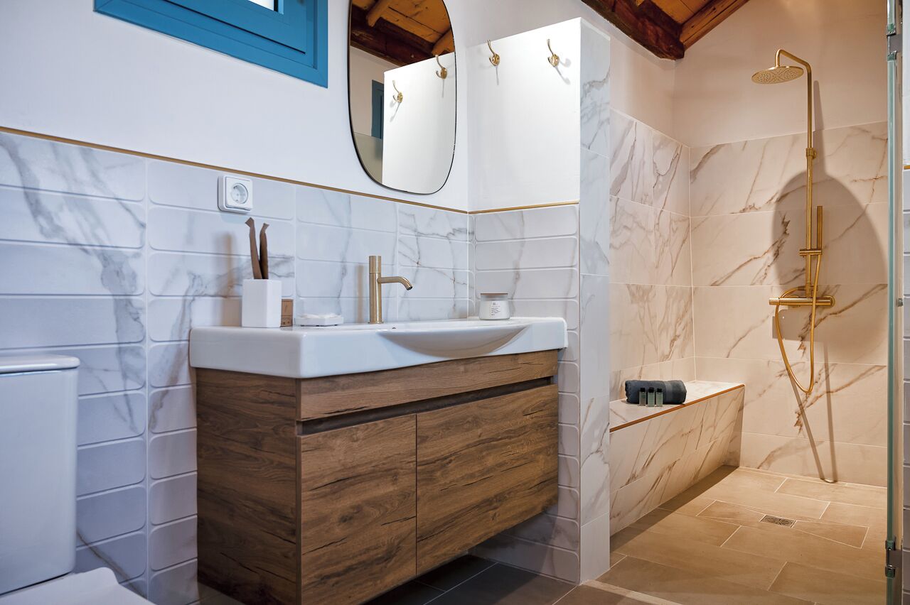 Un baño moderno con lavamanos de mármol, tocador de madera y ducha a ras de suelo.