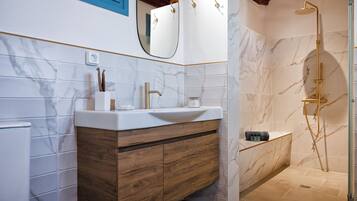 Un baño moderno con lavamanos de mármol, tocador de madera y ducha a ras de suelo.
