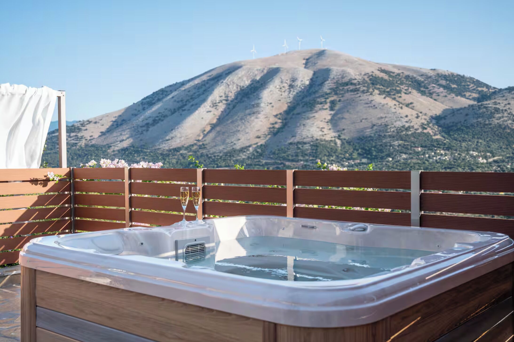 Un jacuzzi con cubierta de madera y vista a las montañas al fondo.