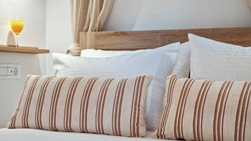 Una cama bien hecha con almohadas a rayas, un cabecero de madera y una mesita de noche con un vaso de jugo de naranja.