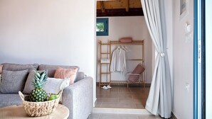 A cozy living room with a grey sofa, a woven basket with a pineapple, and a wooden table. A wooden ladder and clothes rack are visible in the background.