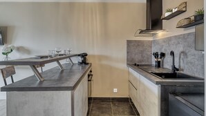 A modern kitchen with a central island, built-in oven, and a stainless steel sink. - Le Cocon 🦋 Apartment in the heart of Thonon les bains ! (Thonon-les-Bains)