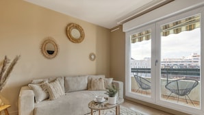 A living room with a beige sofa, a round coffee table, and a view of a cityscape through large windows. - Le Cocon 🦋 Apartment in the heart of Thonon les bains ! (Thonon-les-Bains)