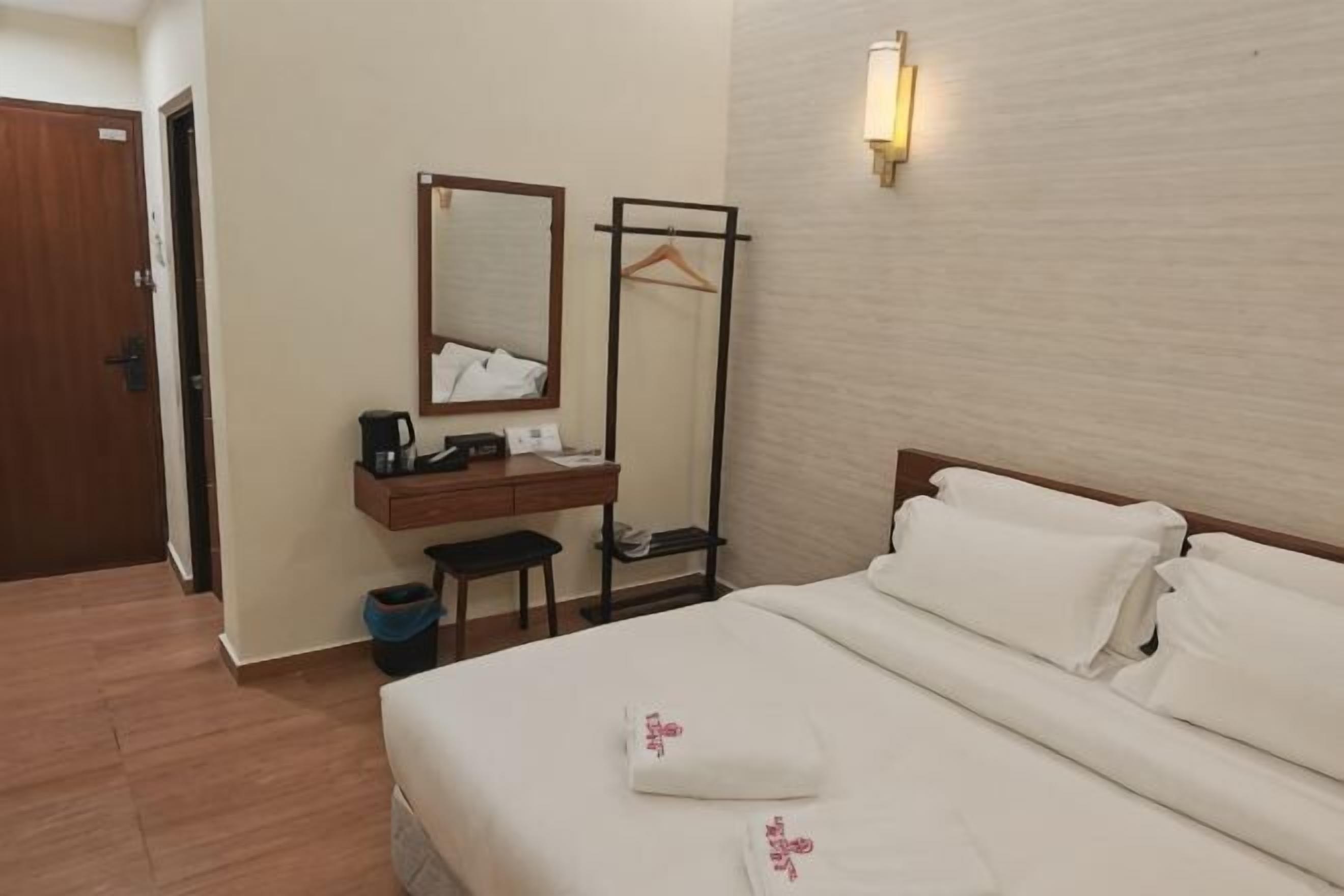 Ein Hotelzimmer mit einem Bett, einem Schreibtisch mit Spiegel, einem Kleiderhaken und einer Wandleuchte.