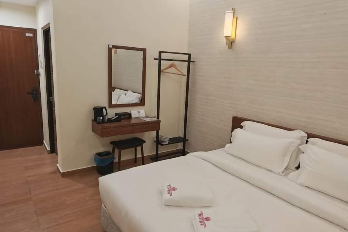 Ein Hotelzimmer mit einem Bett, einem Schreibtisch mit Spiegel, einem Kleiderhaken und einer Wandleuchte.