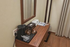 Une chambre d’hôtel avec un bureau en bois, un miroir, une bouilloire, des tasses et une boîte de mouchoirs.