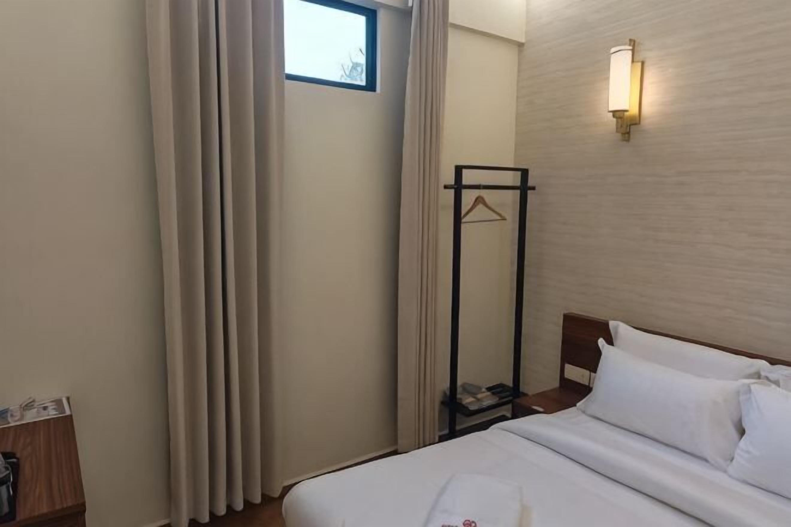 Ein Hotelzimmer mit Bett, Nachttisch, Kleiderhaken und einem Fenster mit Vorhängen.