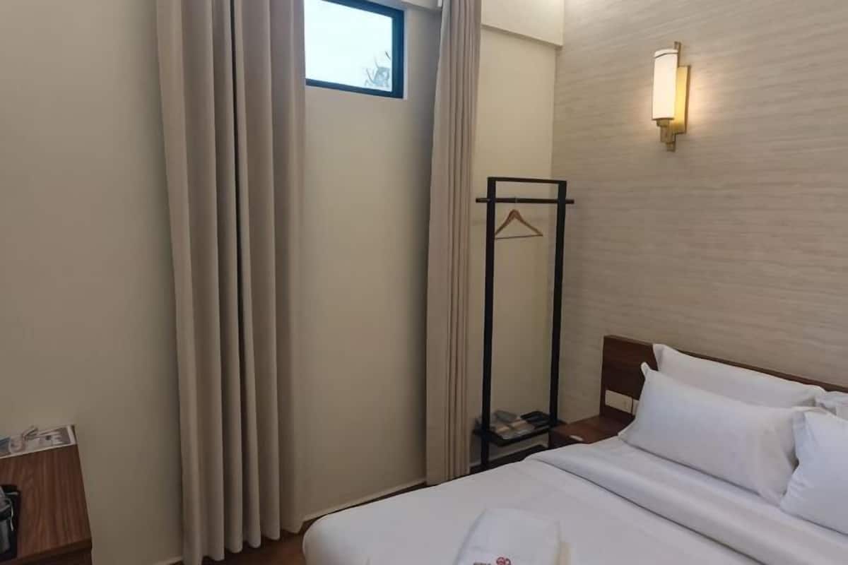Ein Hotelzimmer mit Bett, Nachttisch, Kleiderhaken und einem Fenster mit Vorhängen.