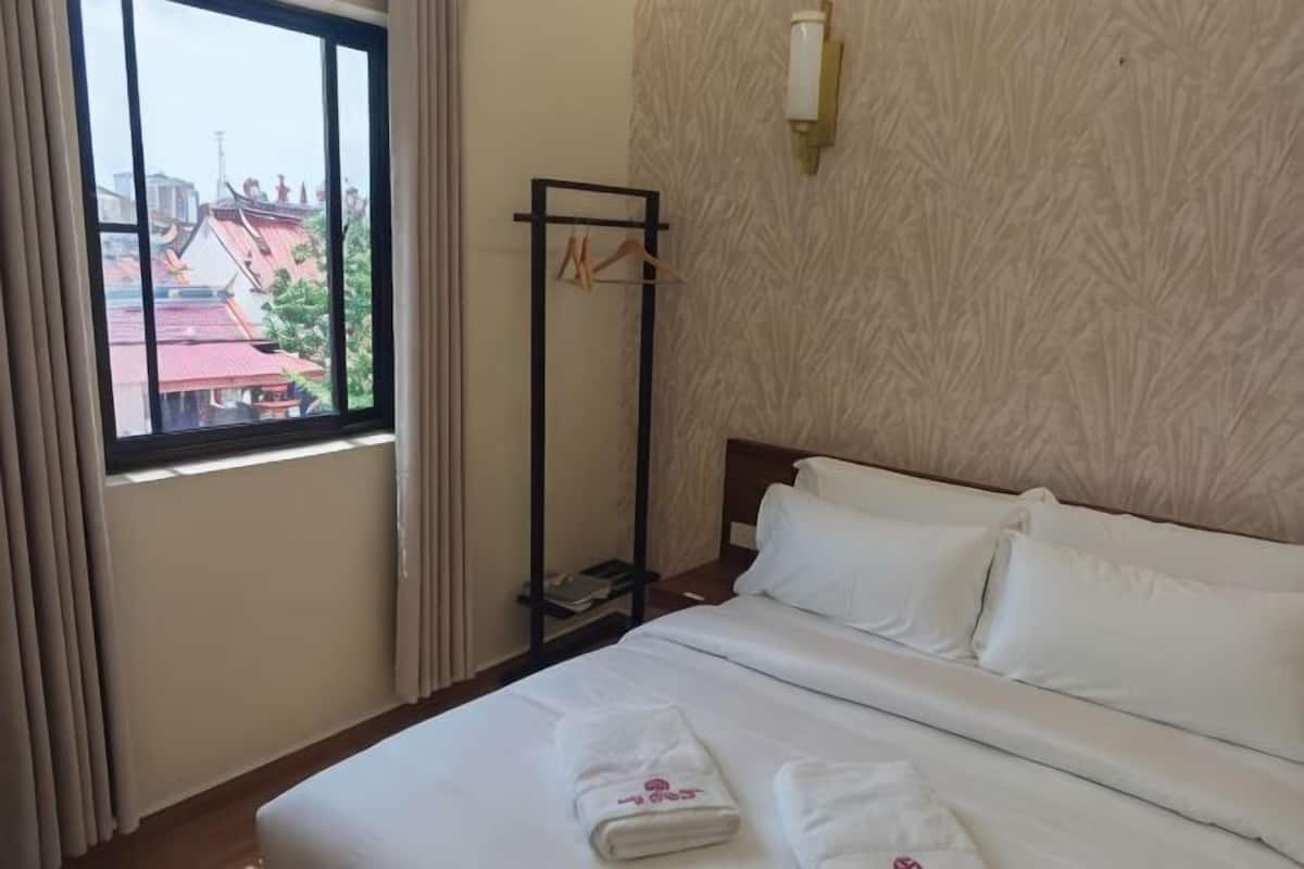 Ein Hotelzimmer mit einem Bett, einem Vorhangfenster, einer Wandleuchte und Blick auf Gebäude.