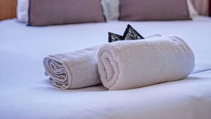 A neatly made bed with a rolled white towel, two pillows, and a window with curtains in the background. - Appartements avenue Gourgaud (Paris)