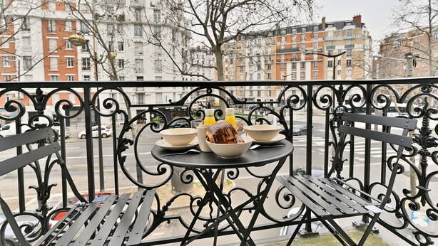 A balcony with a table set for breakfast, featuring bread, a bowl, and a bottle of orange juice. - Appartements avenue Gourgaud (Paris)