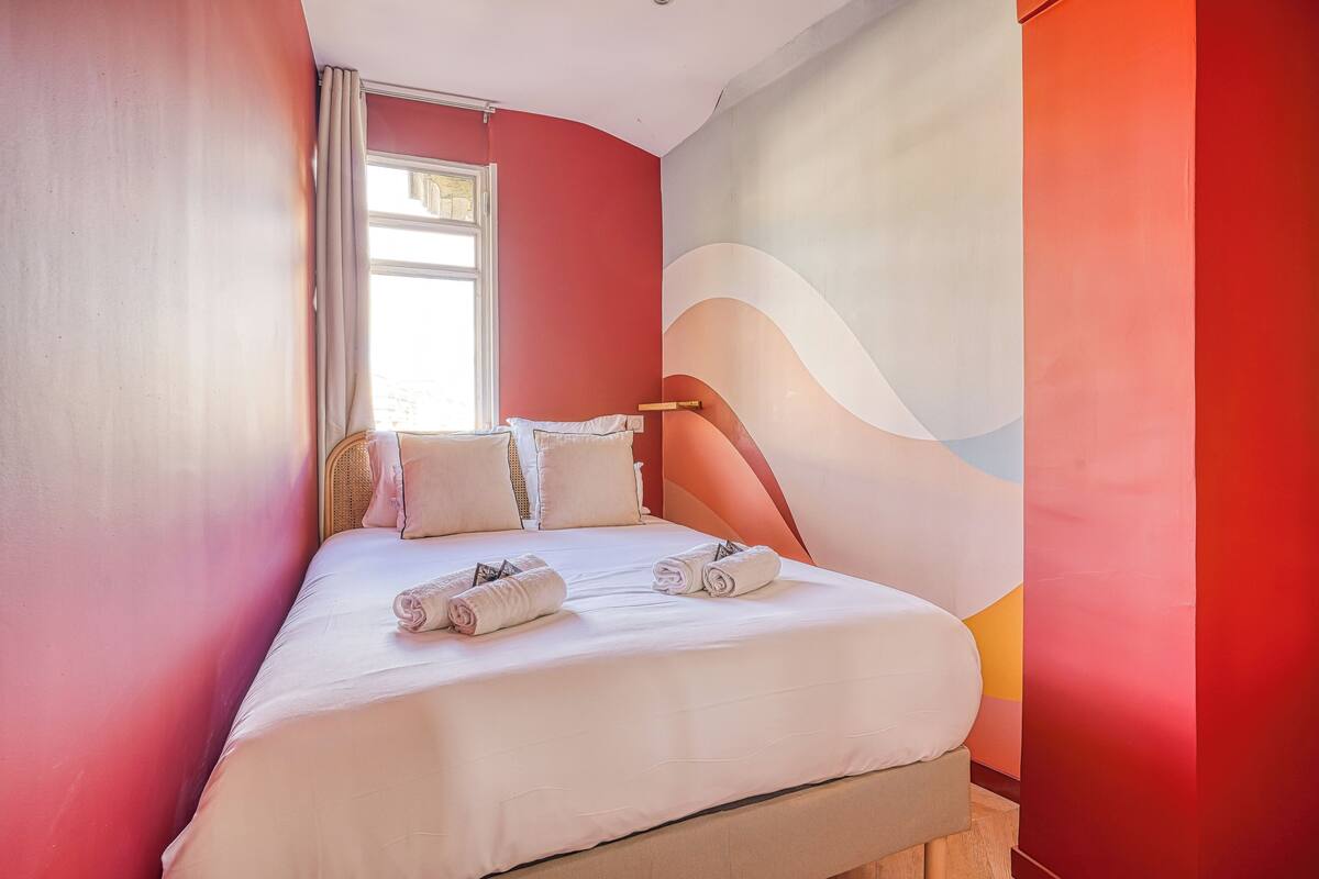 Una habitación de hotel moderna con una cama grande, ropa de cama blanca y un mural abstracto colorido en la pared.