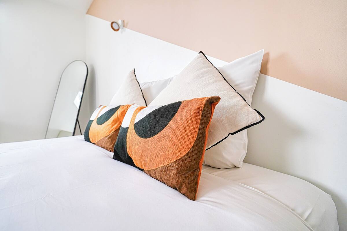 Una cama bien hecha con ropa blanca y dos almohadones decorativos.