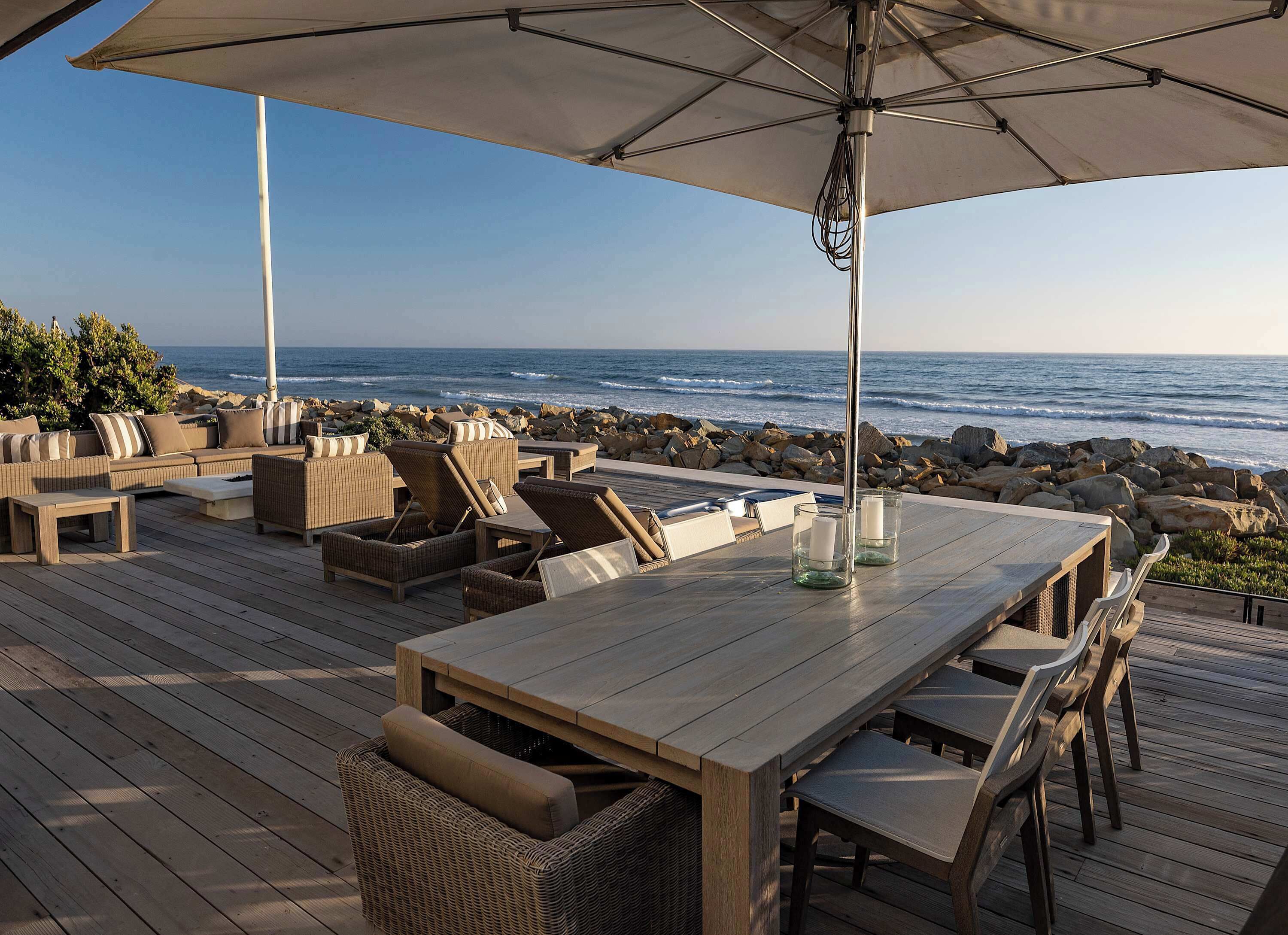 Um deck de madeira com móveis de exterior, uma mesa e um guarda-sol.