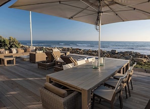 Um deck de madeira com móveis de exterior, uma mesa e um guarda-sol.