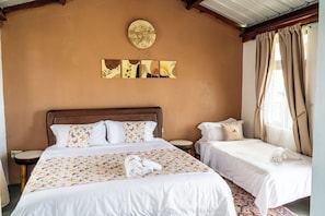 Habitación de hotel con una cama grande, dos camas más pequeñas, un adorno redondo en la pared y una ventana con cortinas.