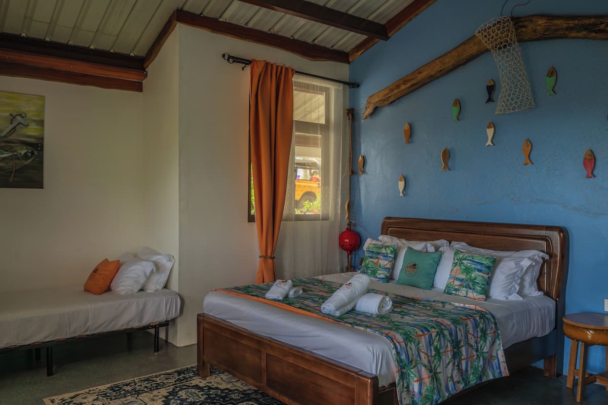 Un dormitorio con una cama, una cama adicional, una ventana con cortinas y una pared decorada con motivos de peces.