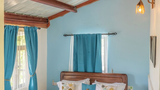 A bedroom with a wooden bed, a ceiling fan, and a window with curtains. - Baz-Art Eco Guest House (Rodrigues Island)