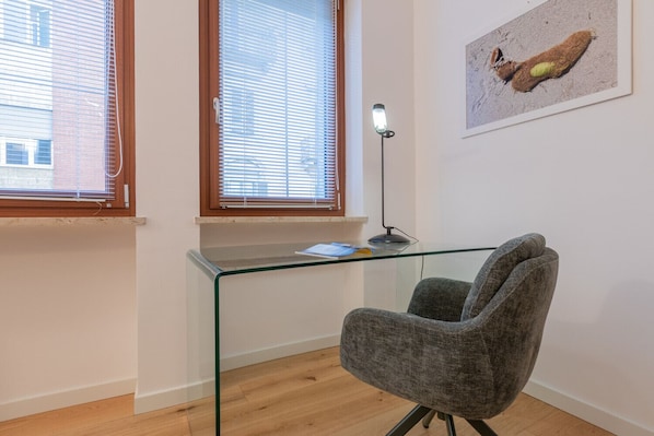 Une pièce moderne avec un bureau en verre, un fauteuil gris et une lampe sur pied.