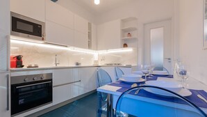 A modern kitchen with white cabinets, a built-in microwave, and a stove. There is a dining table with blue chairs and a set of wine glasses. - Ormea Cobalto Apartment by Wonderful Italy (Turin)