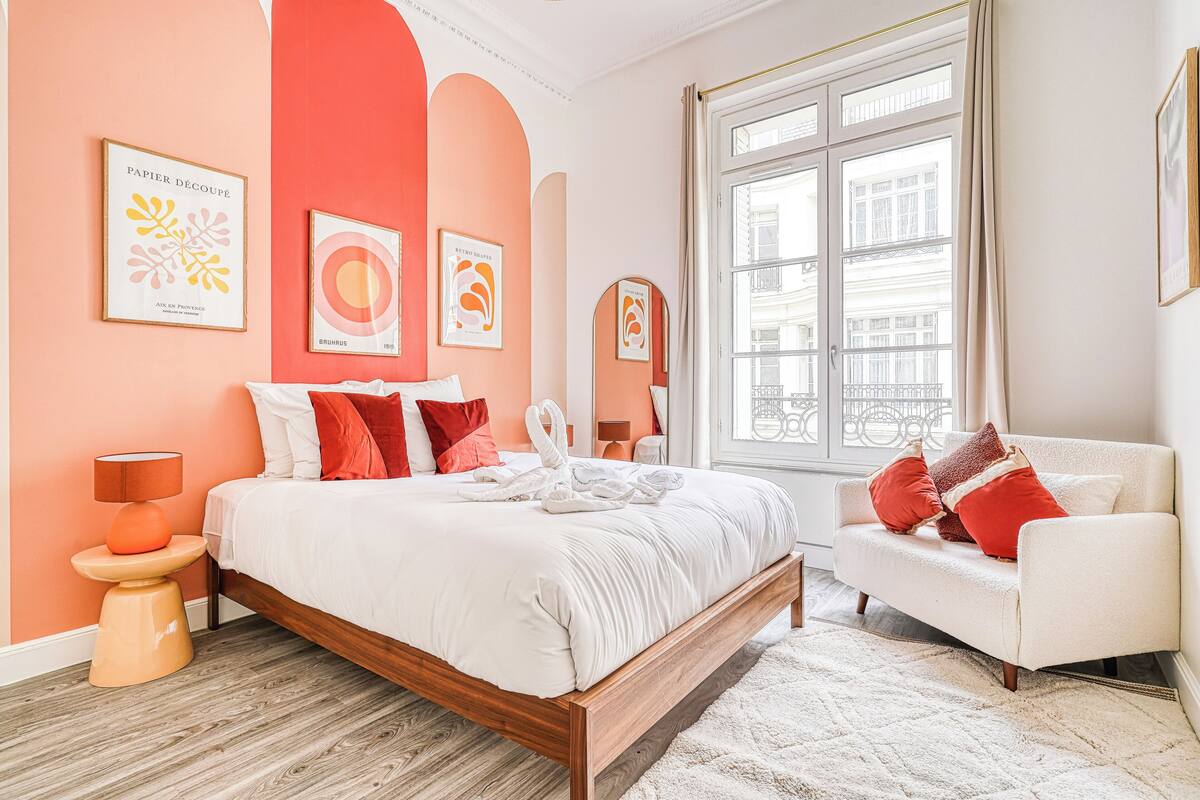A bedroom with a bed, a sofa, a window, and artwork on the walls.
