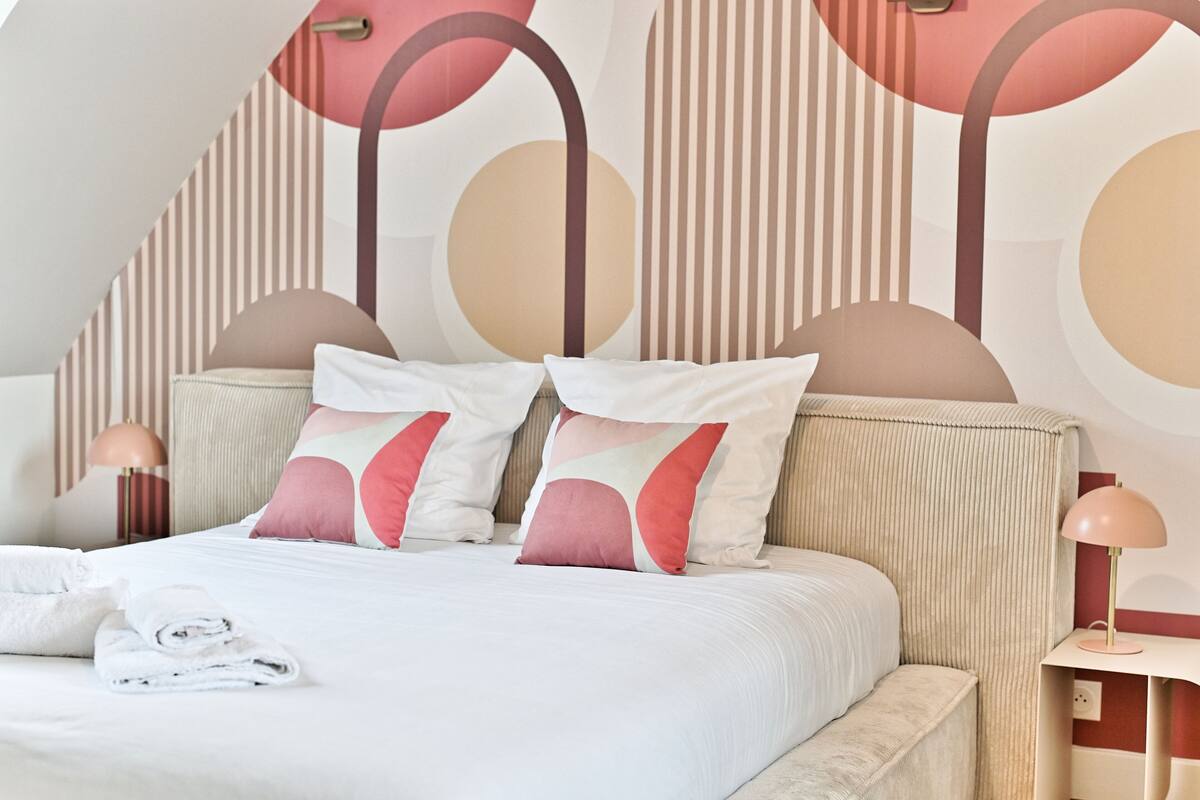 A modern bedroom with a bed, pillows, a bedside table, and a lamp.