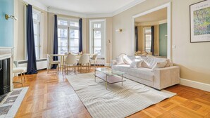 Ett vardagsrum med en soffa, ett soffbord i glas, en öppen spis och en matplats med stolar och ett bord.