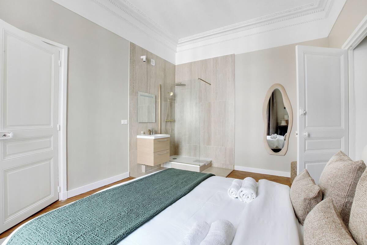 A hotel room with a large bed, a bathroom with a mirror, and a wooden floor.