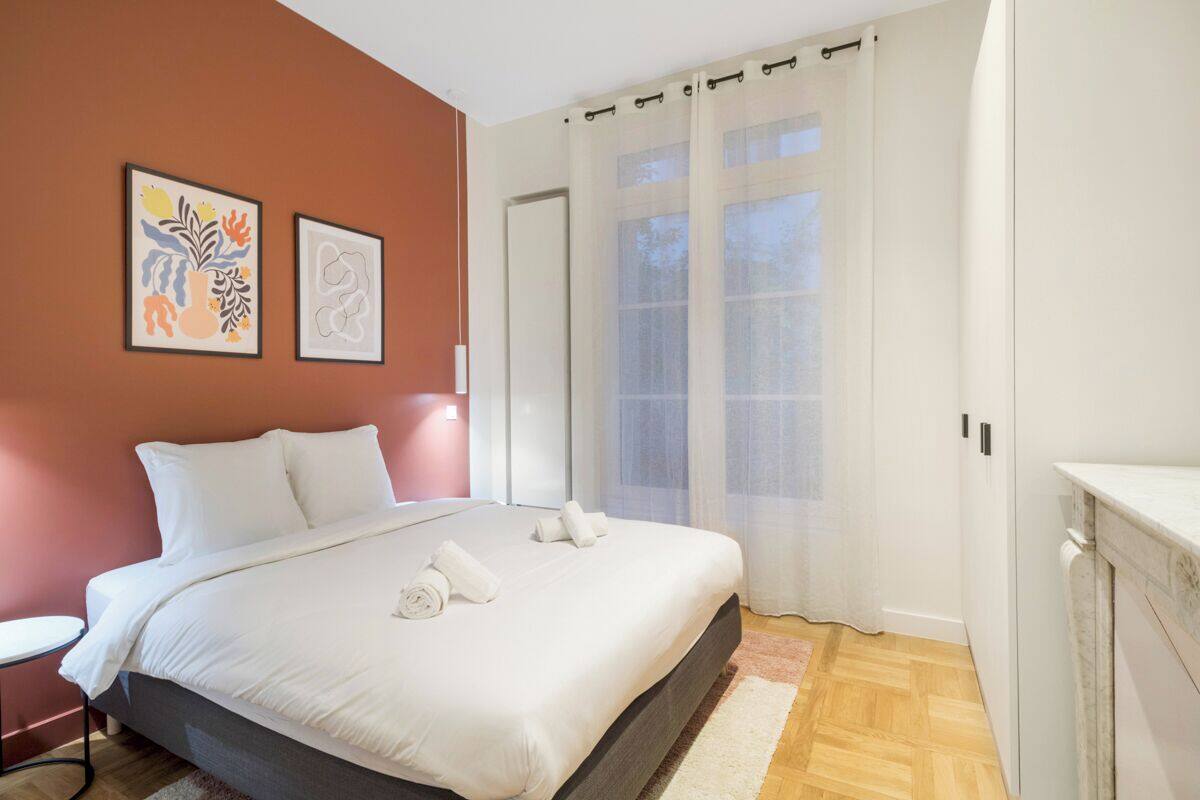 A bedroom with a bed, a bedside table, a chair, and a window with curtains.