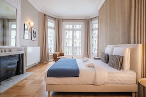 Habitación de hotel con una cama grande, una chimenea, un balcón con barandilla y vistas a edificios.