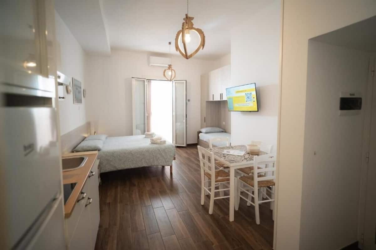 Habitación pequeña con cama, una mesita y una silla. Ventana con vista al exterior.