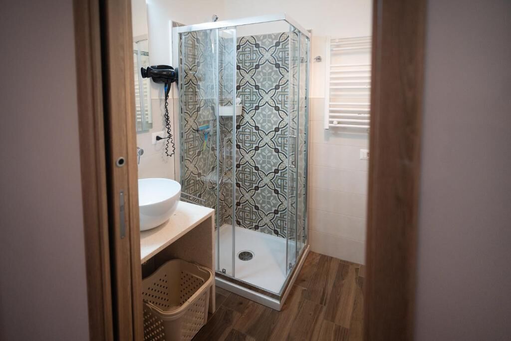 Een badkamer met een douchecabine van glas, een witte wastafel en een betegelde spatwand met een patroon.