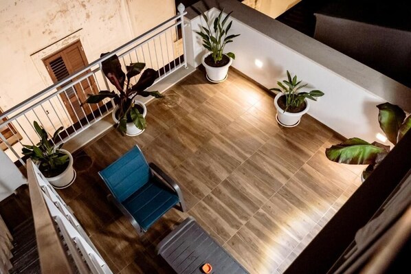 Un ampio balcone con pavimento in legno, piante in vaso e una sedia blu.