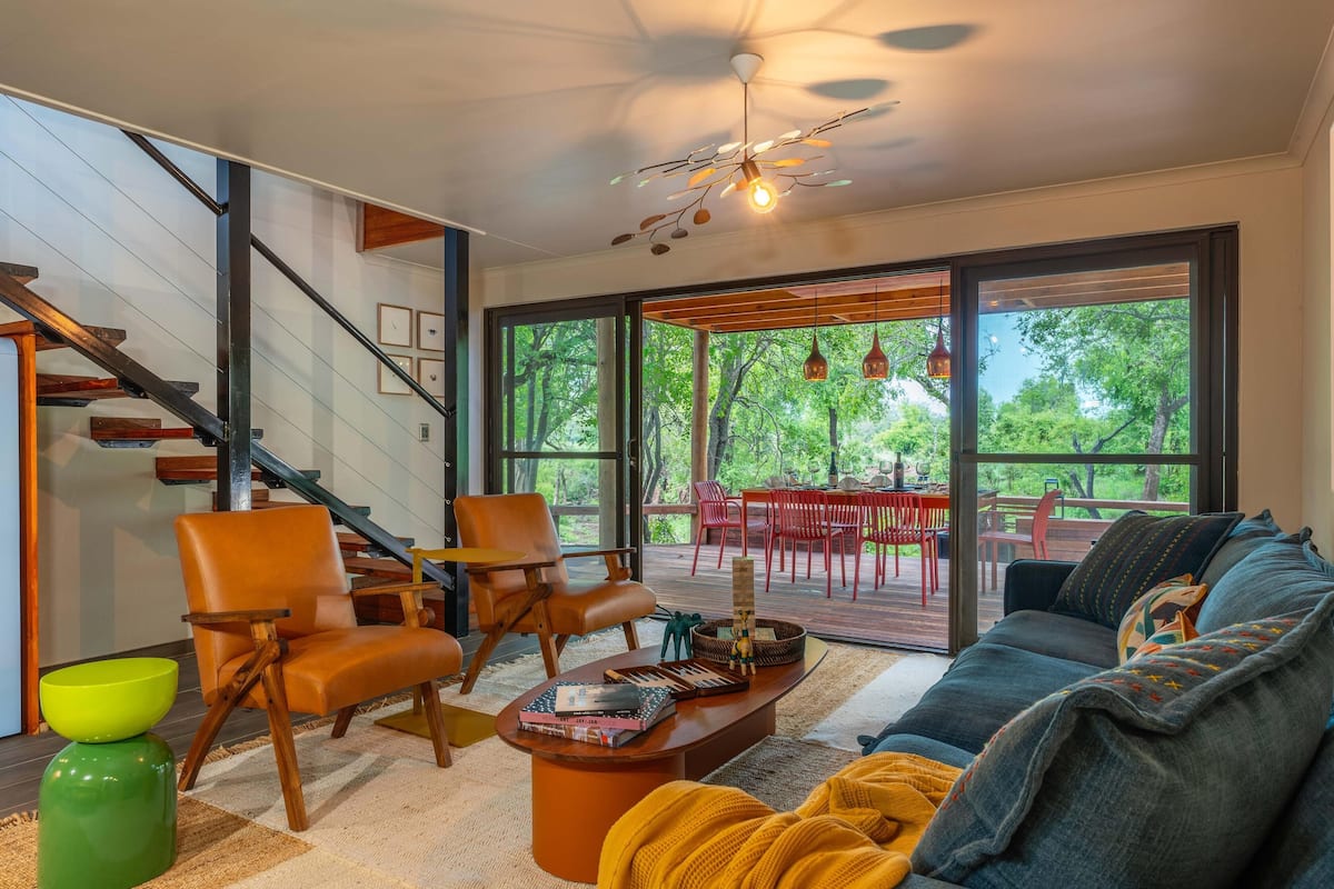 A modern living room with a staircase, a large window with a view of trees, a sofa, and a coffee table.