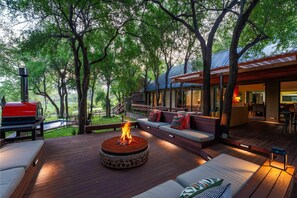 Een terras met vuurplaats, buitenmeubels en uitzicht op een modern huis.