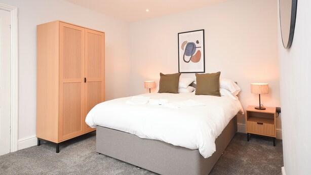 Une chambre à coucher avec un grand lit, une armoire, une table de chevet avec une lampe et un tableau encadré au mur.