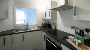 Une cuisine moderne avec des meubles blancs, un plan de travail noir, une fenêtre et un grille-pain.