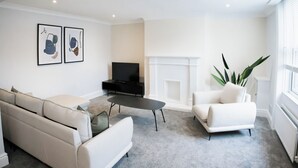 Un salon moderne avec un canapé, une table basse et un téléviseur. On y trouve également une cheminée et une plante.