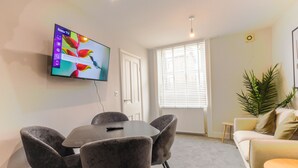Un salon moderne doté d’un téléviseur à écran plat, d’une table à manger avec des chaises, d’un canapé et d’une petite table d’appoint.
