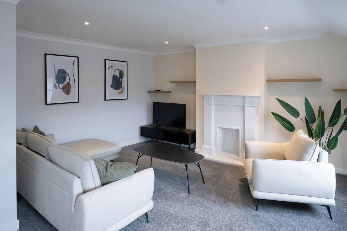 Un salon moderne avec un canapé, un fauteuil et une table basse. On y trouve également un téléviseur à écran plat et une cheminée.