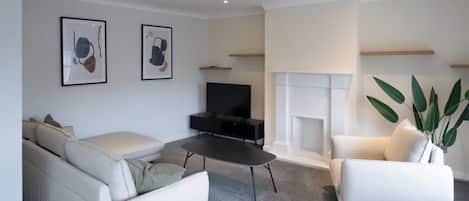 A modern living room with a sofa, armchair, and a coffee table. There is a flat-screen TV and a fireplace.
