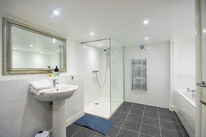 A modern bathroom with a glass-enclosed shower, a white sink with a mirror, and a bathtub. - Boughton House Apartments by Guestz (Chester)