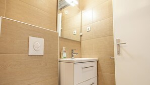 A bathroom with wooden walls, a white sink, a mirror, and a toilet. - Cozy Apartment for 3 Near Lugner City (Vienna)