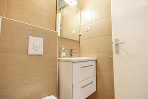 A bathroom with wooden walls, a white sink, a mirror, and a toilet. - Cozy Apartment for 3 Near Lugner City (Vienna)