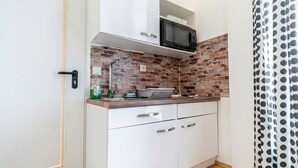 A compact kitchen with white cabinets, a microwave, and a brick backsplash. - Cozy Apartment for 3 Near Lugner City (Vienna)