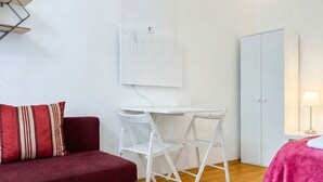 A room with a red sofa, a white foldable table, a white wardrobe, and a wall-mounted light fixture. - Cozy Apartment for 3 Near Lugner City (Vienna)