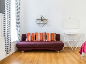 A room with a purple sofa, a small white desk, and a whiteboard on the wall. - Cozy Apartment for 3 Near Lugner City (Vienna)