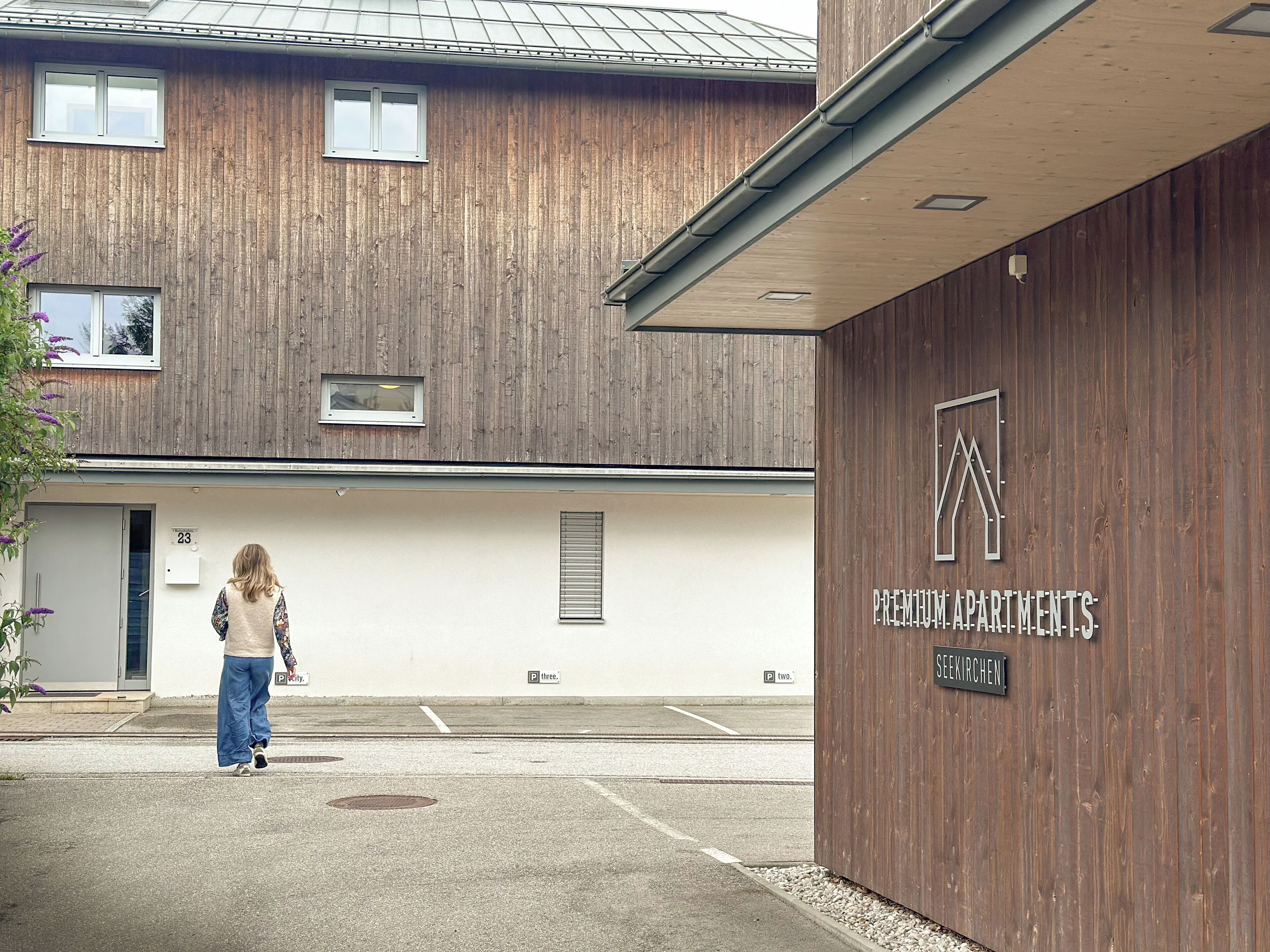 A building with a wooden facade, a sign for "Premium Apartments," and a parking area with marked spaces.