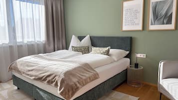 A neatly made bed with a green headboard, a bedside table with a lamp, and two framed quotes on the wall.